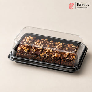 Chocolate nut bars in a clear plastic clamshell container with a black tray, photographed on a warm beige background. The Bakeyy logo is visible in the top right corner.