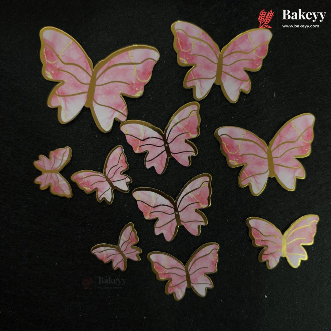 Pink and white marbled butterfly-shaped embellishments with gold borders, arranged on a black background. The Bakeyy brand logo is visible in the top right corner.