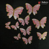 Pink and white marbled butterfly-shaped embellishments with gold borders, arranged on a black background. The Bakeyy brand logo is visible in the top right corner.