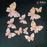Ten butterfly-shaped baking decorations with pink and white marbled wings and gold edges, scattered on a dark textured background. The Bakeey brand logo is visible in the top right corner.