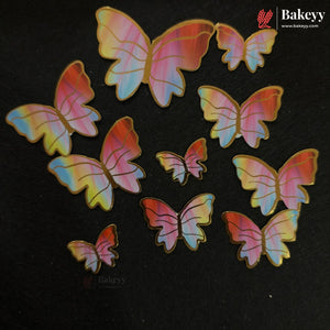 A set of iridescent butterfly-shaped craft embellishments in various sizes, displayed on a black background. The butterflies feature a holographic finish shifting between pink, yellow, and blue, with gold-colored borders.