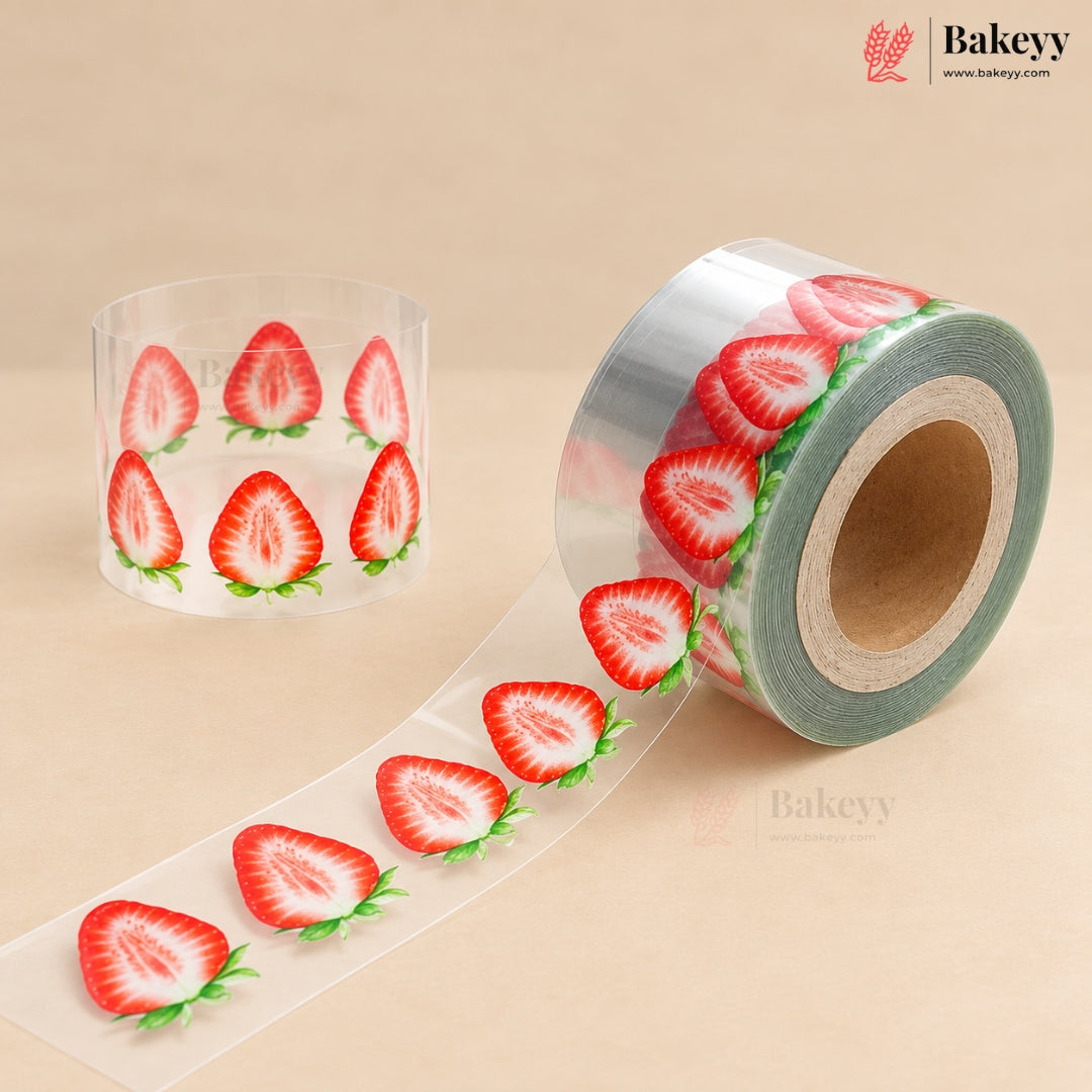 A roll of clear adhesive tape printed with red strawberry slices and green leaves, shown unspooled alongside a standing spool on a beige background. The Bakeyy brand logo is visible in the top right corner.