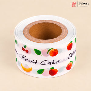 A roll of white bakery tape printed with colorful illustrations of fruits (cherries, peaches, bananas, apples) and the words 'Fruit Cake' and 'Delicious', shown on a beige background with a Bakeyy logo in the top right corner.
