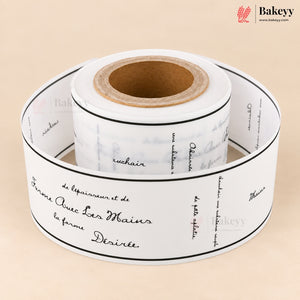 A roll of white bakery labels printed with elegant black cursive script and thin black border lines, displayed on a warm beige background. The Bakeey brand logo is visible in the top right corner.
