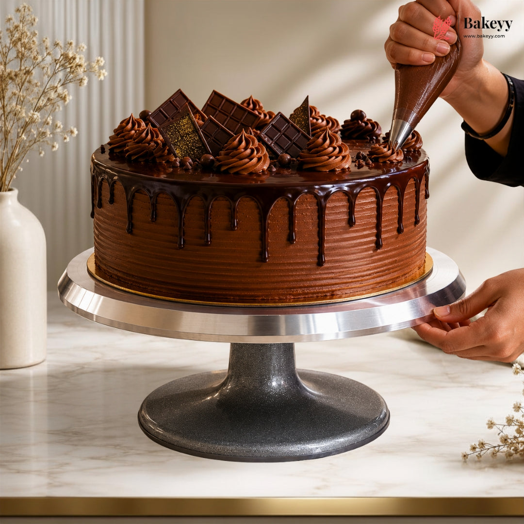 Chocolate cake being decorated with chocolate ganache on a marble surface.