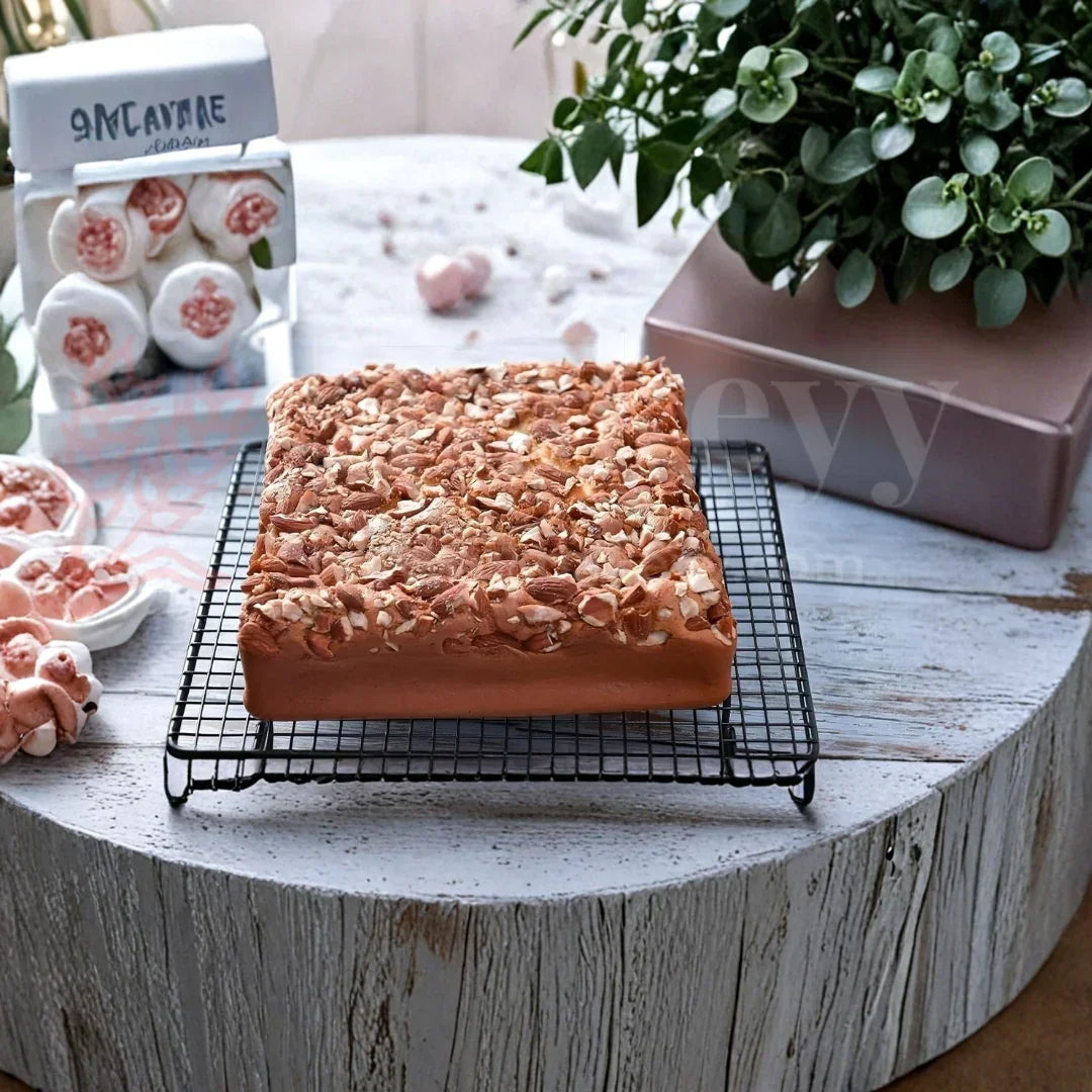 Square nut-topped cake on cooling rack, baking supplies in background, Bakeyy baking products