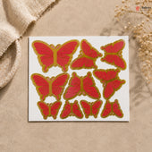 Red butterfly stickers with gold edges on a white card, placed on a beige surface.