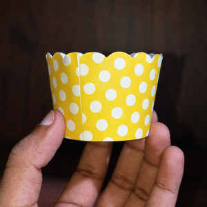 Yellow cupcake liner with white polka dots held in a hand against a dark background
