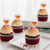 Red velvet cupcakes with cream cheese frosting and heart-shaped alcohol bottles on a white surface.