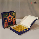A blue and gold bakery gift set including an open box of individually wrapped pastries and a matching decorative gift bag, displayed on a neutral light gray background.