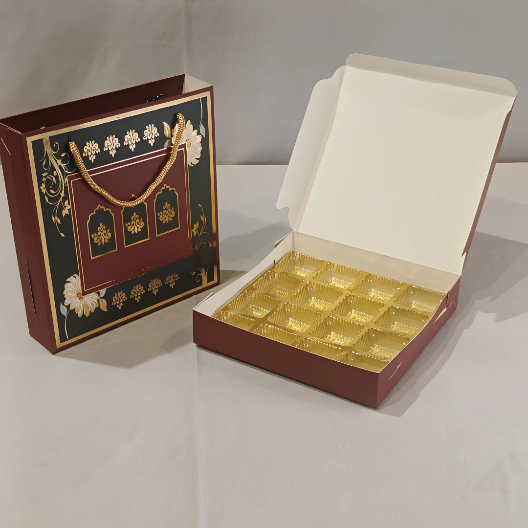 A luxury gift box set featuring a closed decorative maroon and gold paper bag with white floral accents, next to an open matching box containing twelve gold foil-lined compartments.
