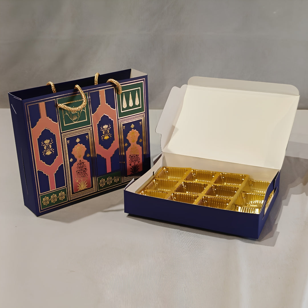 A navy blue gift box with gold foil compartments shown open next to a matching decorative gift bag with gold rope handles, on a light gray background.