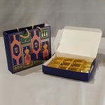 A navy blue gift box with gold foil compartments shown open next to a matching decorative gift bag with gold rope handles, on a light gray background.