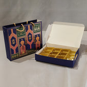 A navy blue gift box with gold foil compartments shown open next to a matching decorative gift bag with gold rope handles, on a light gray background.
