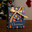 Christmas gift box with colorful tree pattern and gold ribbon on a wooden surface.