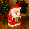 Santa Claus-themed gift box with a red ribbon on a wooden floor with Christmas decorations in the background.