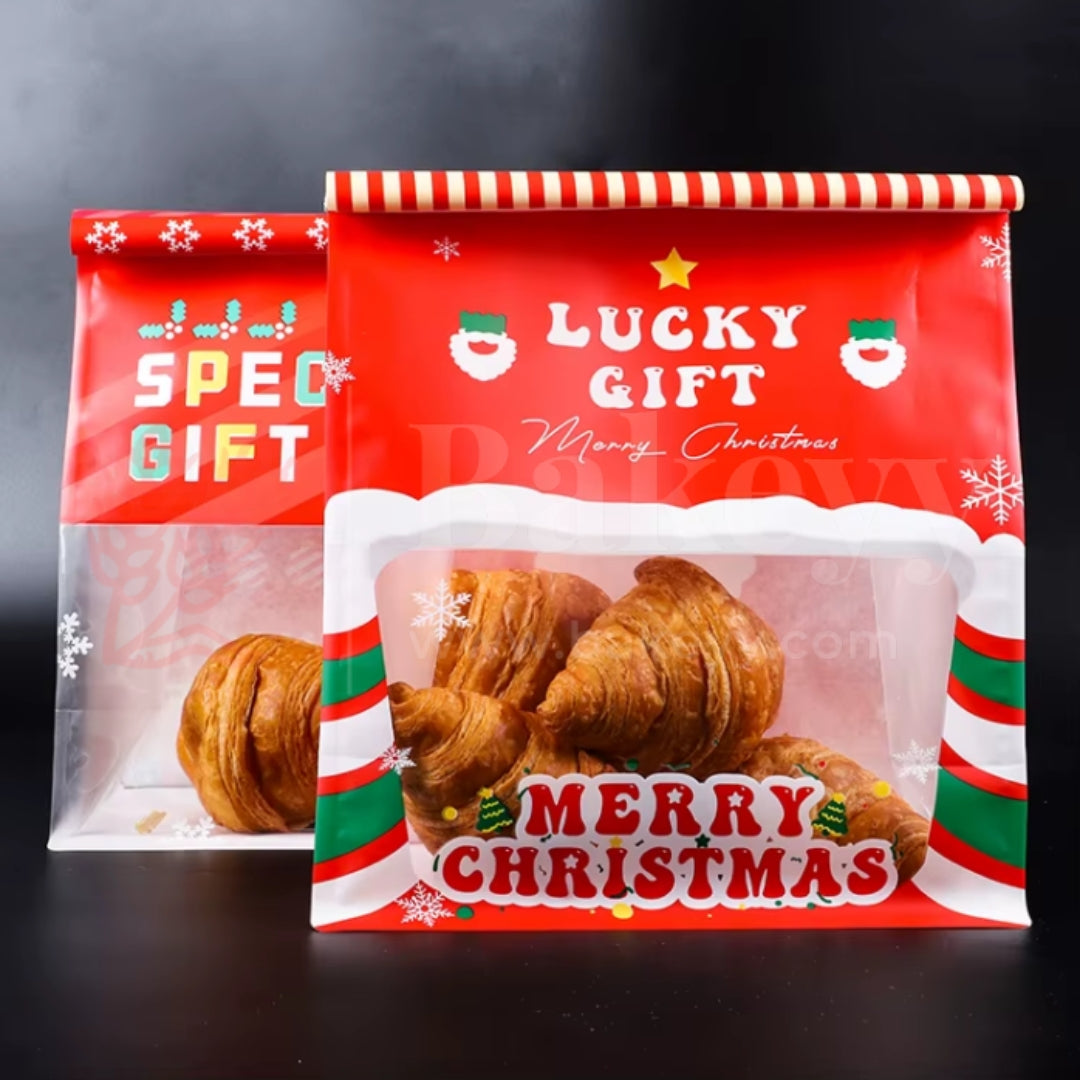 Two Christmas-themed gift bags with croissants inside on a dark background