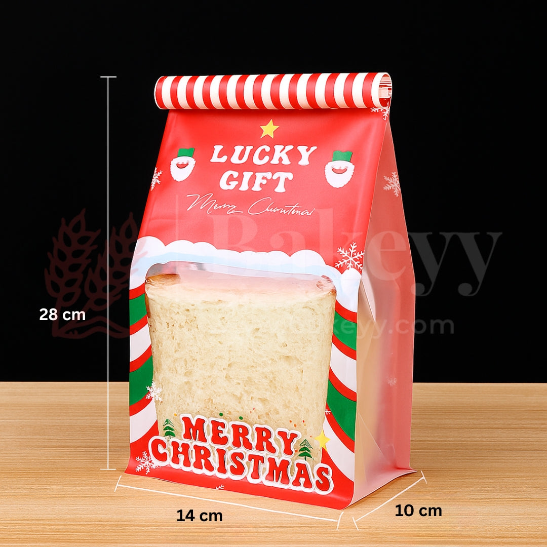 Red Christmas-themed gift bag with a sandwich inside, on a wooden surface.