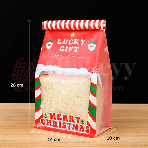 Red Christmas-themed gift bag with a sandwich inside, on a wooden surface.