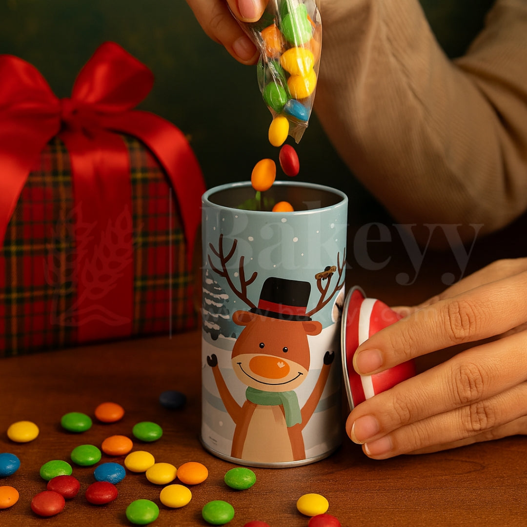 Person pouring colorful candies into a mug with a reindeer design, next to a gift box.