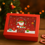 Red Christmas gift box with Santa Claus illustration on a wooden surface with festive decorations.