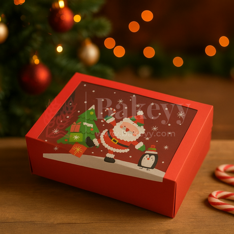Red Christmas-themed gift box with Santa Claus design on a wooden surface with blurred Christmas tree and lights in the background.