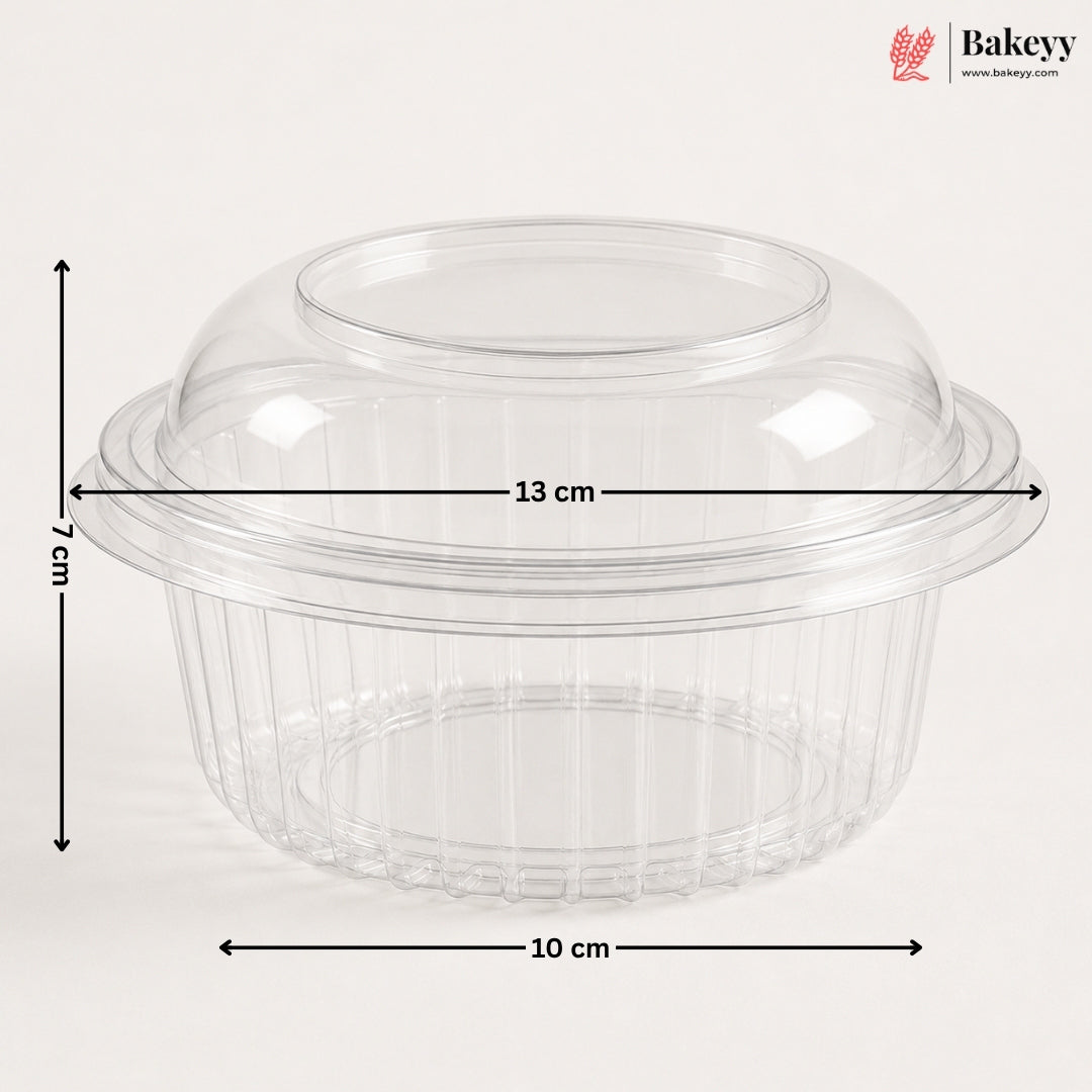 Clear plastic dome lid with a flared rim and ribbed base, shown with dimension arrows and labels indicating 13 cm width, 10 cm base diameter, and 7 cm height on a light gray background. Bakeyy logo appears in the top right.