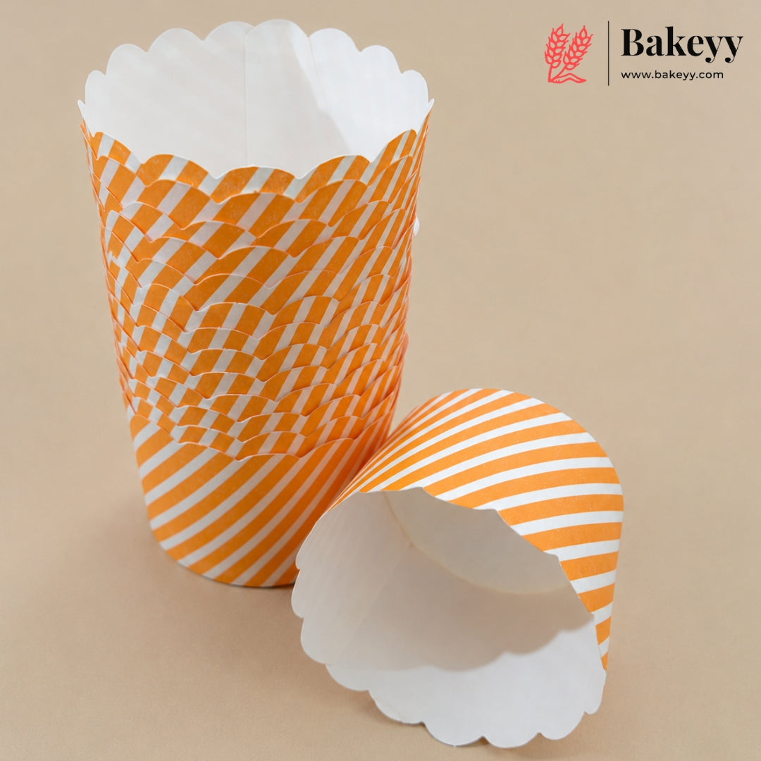 Two white paper cupcake liners with orange patterns, one standing upright and the other lying on its side, on a beige background. The Bakeyy logo is visible in the top right corner.
