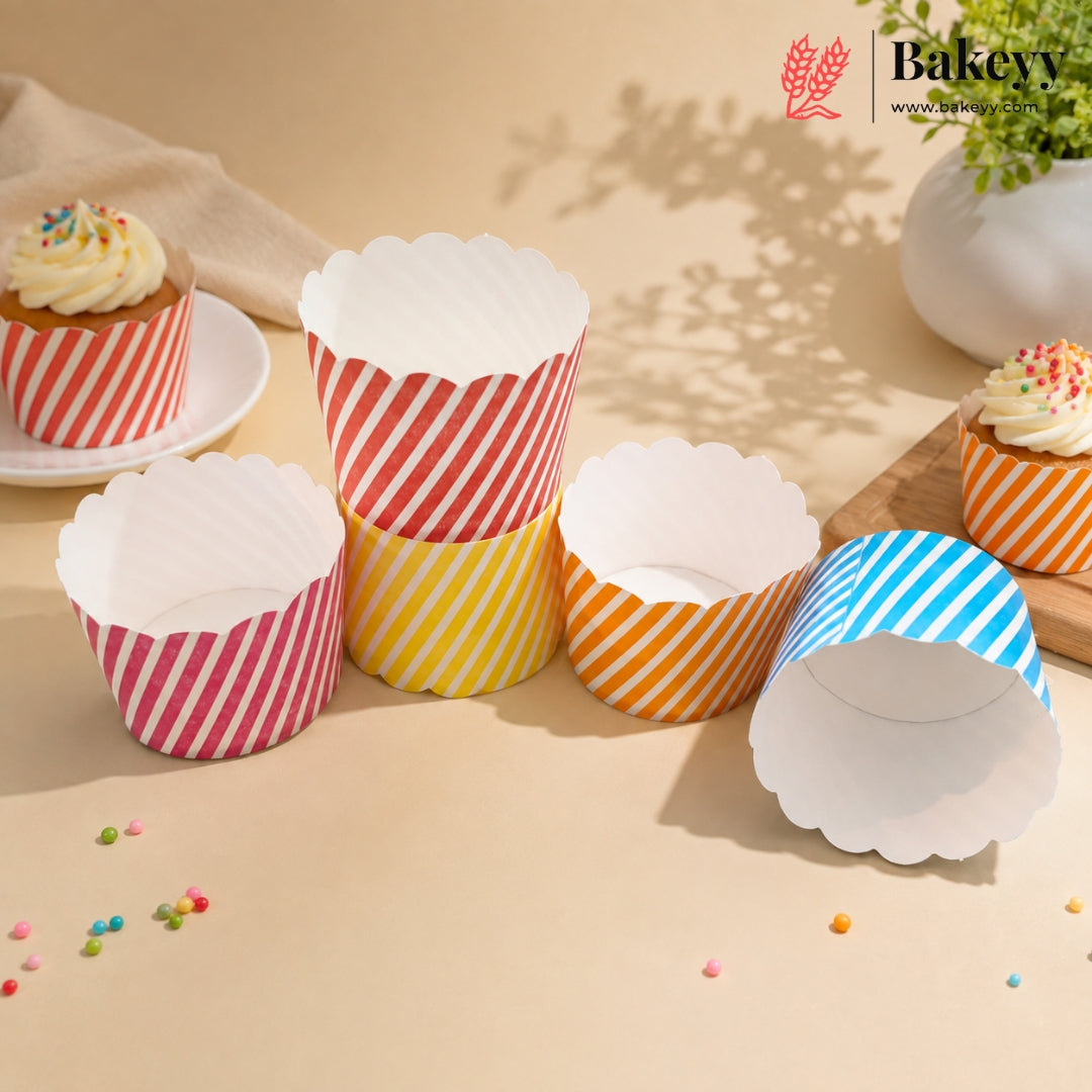 Six paper cupcake liners in red, yellow, orange, and blue striped patterns with white scalloped edges, displayed on a beige surface with cupcakes in the background.