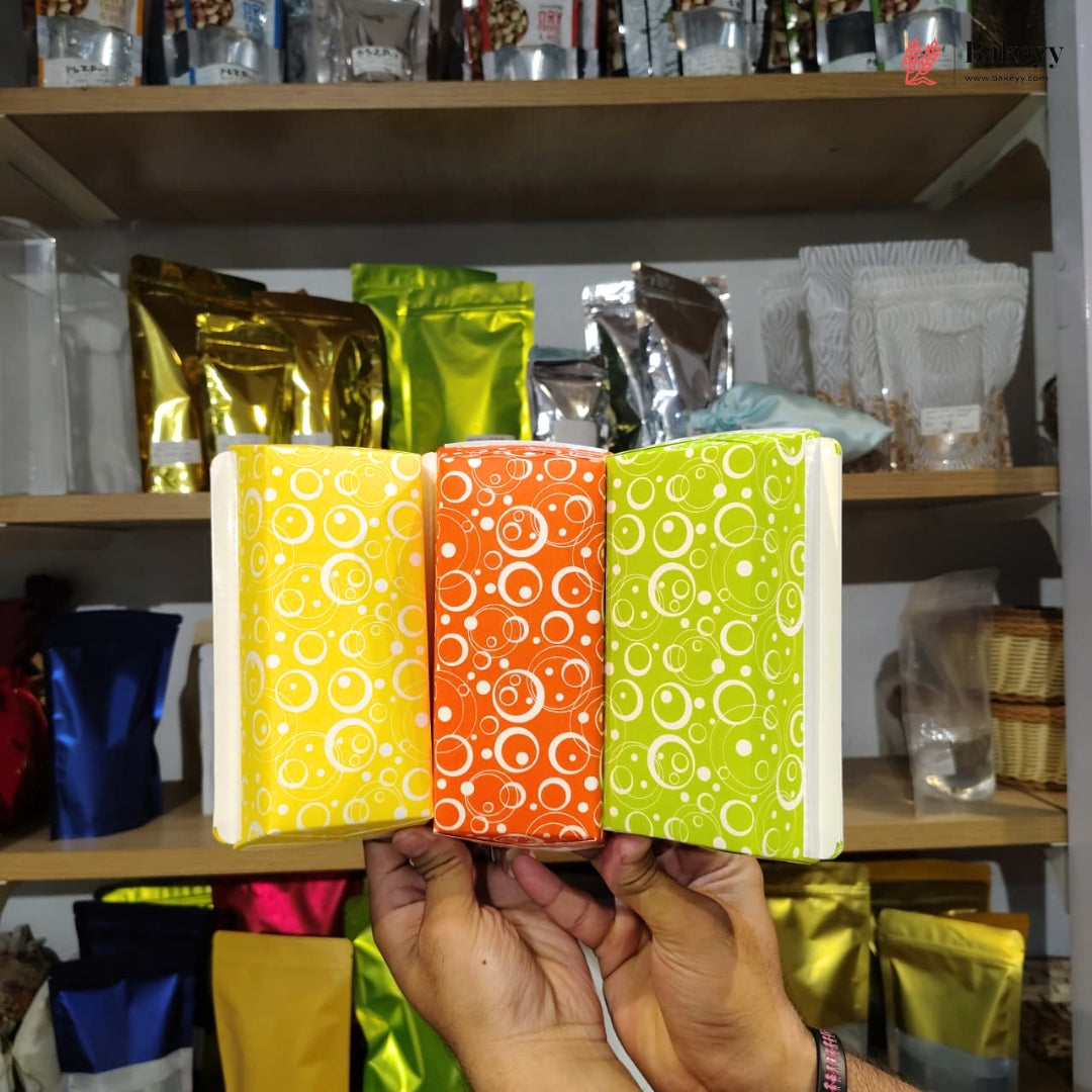 Three colorful packages with circular patterns held in front of a shelf with various other packages.