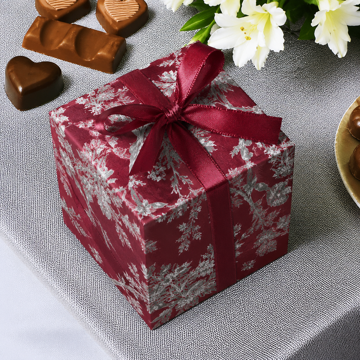 Gift box with red ribbon on a gray surface with chocolates and flowers