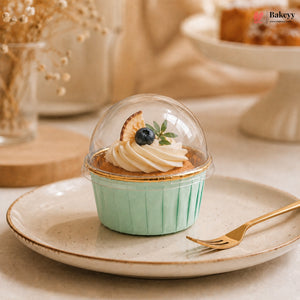 Cupcake in a green case with a clear dome on a plate, featuring the Bakey brand.