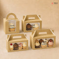 Four cardboard cupcake boxes with clear windows displaying cupcakes, on a beige background.