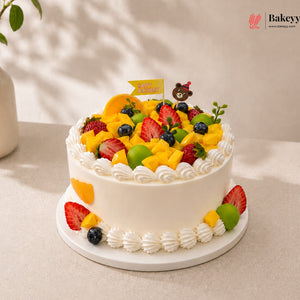 Fruit cake with white frosting and colorful fruits on a light background, featuring the brand 'Bakeyy'.