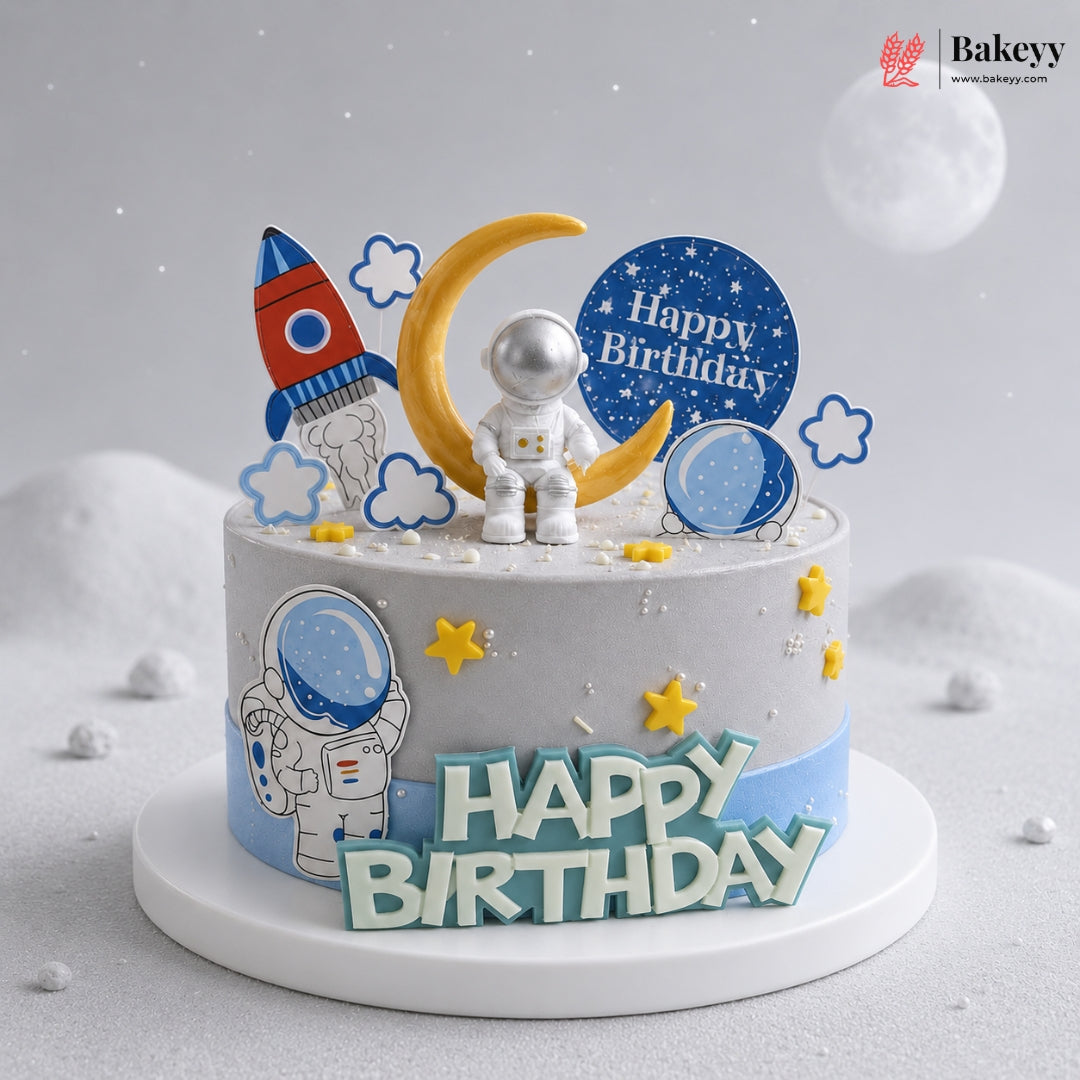 Space-themed birthday cake with astronaut, rocket, and moon decorations on a light gray background.