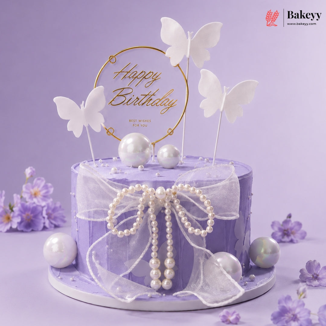Purple birthday cake with butterfly toppers and pearl decorations on a purple background, featuring the Bakeyy brand.