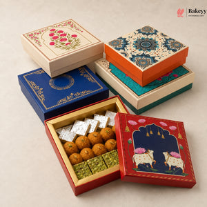 Five decorative gift boxes for sweets are arranged on a light beige background. One red box is open, showing round golden-brown laddoos and green pistachio-filled squares, while another open box shows white sugar cubes.