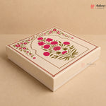 A square cream-colored bakery gift box with a lid decorated with a pink floral design and green leaves, set against a matching beige background.
