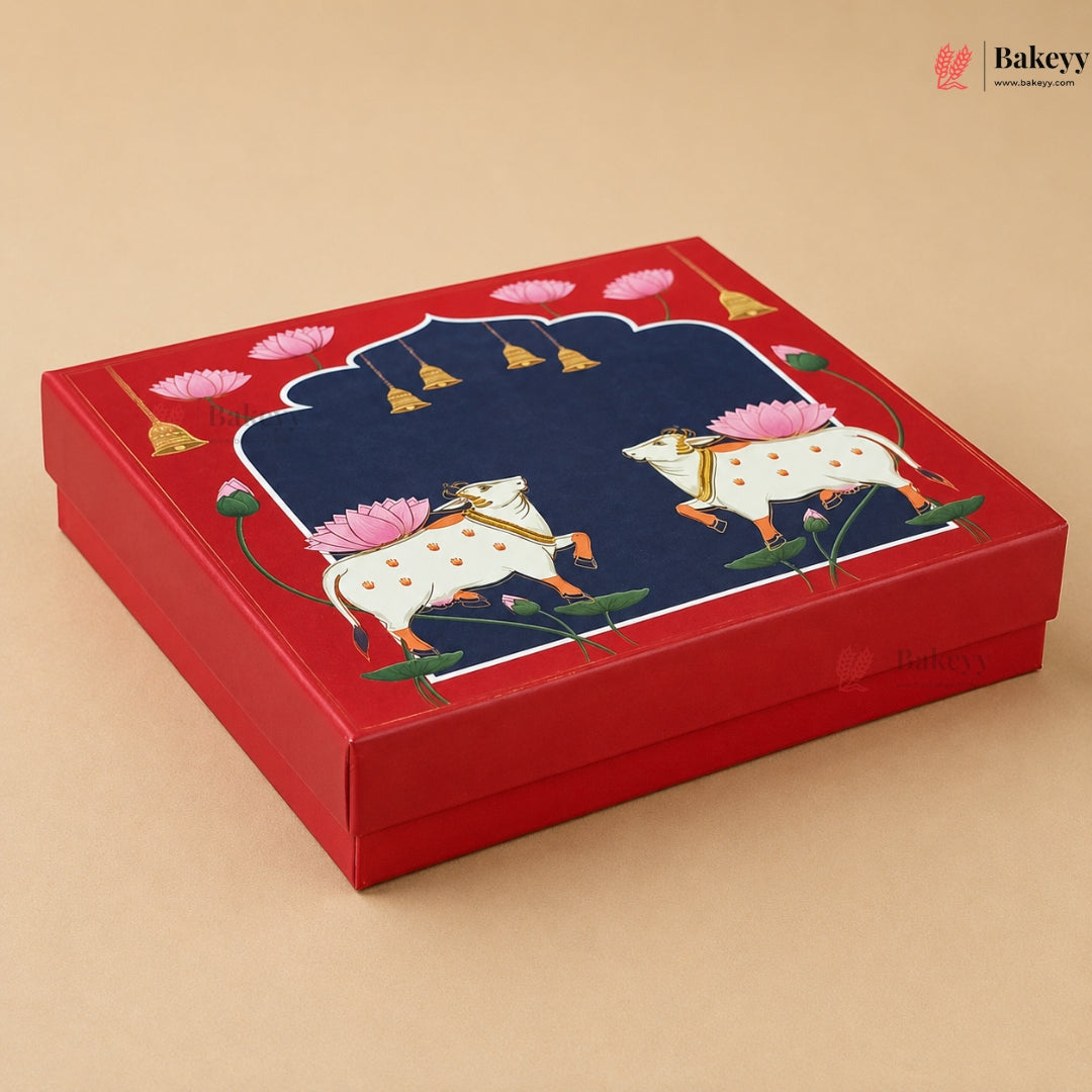 A square red gift box with a lid featuring a detailed illustration of two white cows with pink lotus flowers on a beige background.