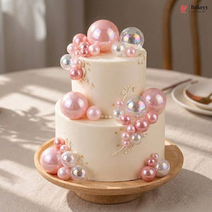 Two-tier cake decorated with pink and clear balloons on a wooden stand.