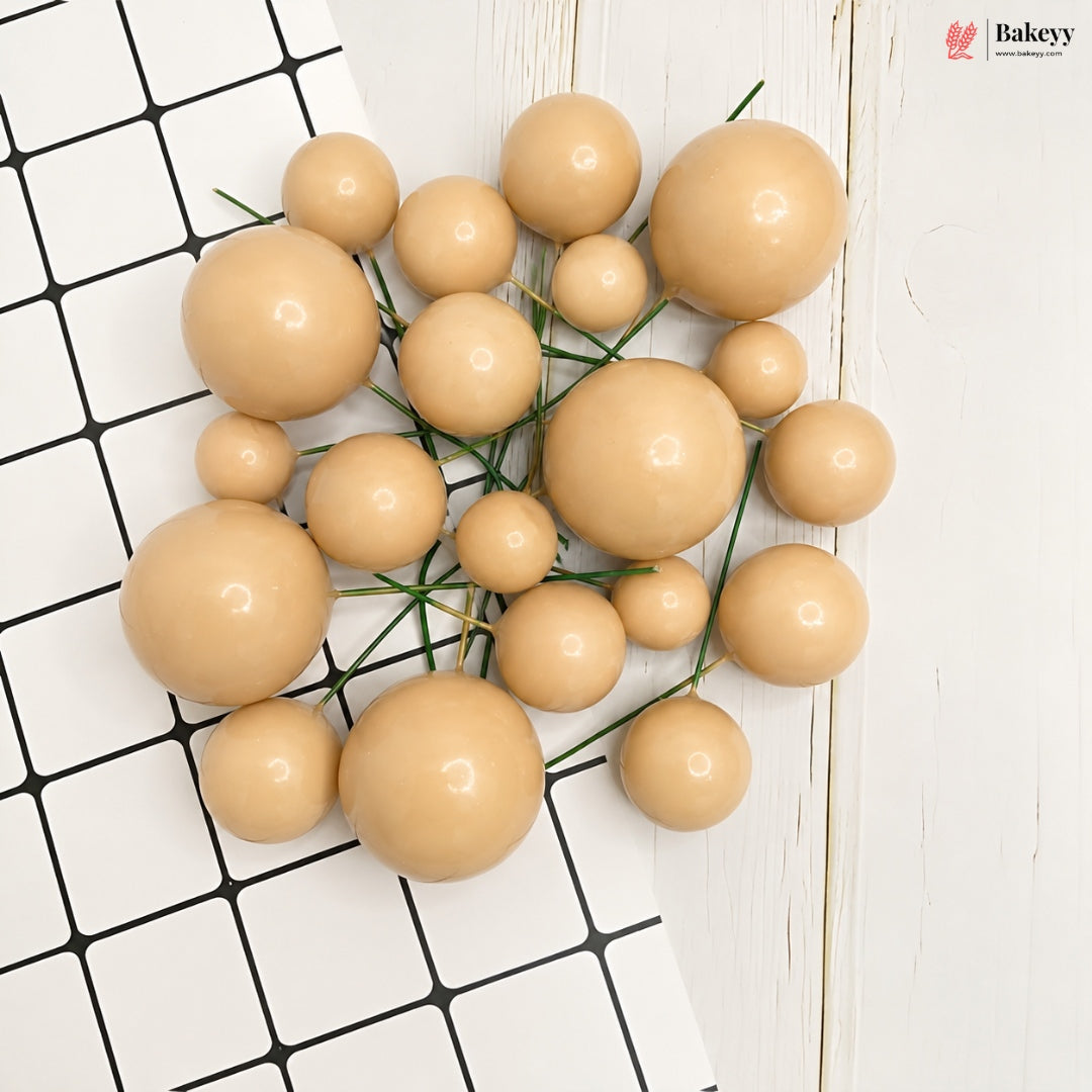 A set of glossy, peach-beige decorative foam balls of various sizes, strung together on thin green wire, arranged on a split background of black-and-white checkered tiles and a white wood panel.