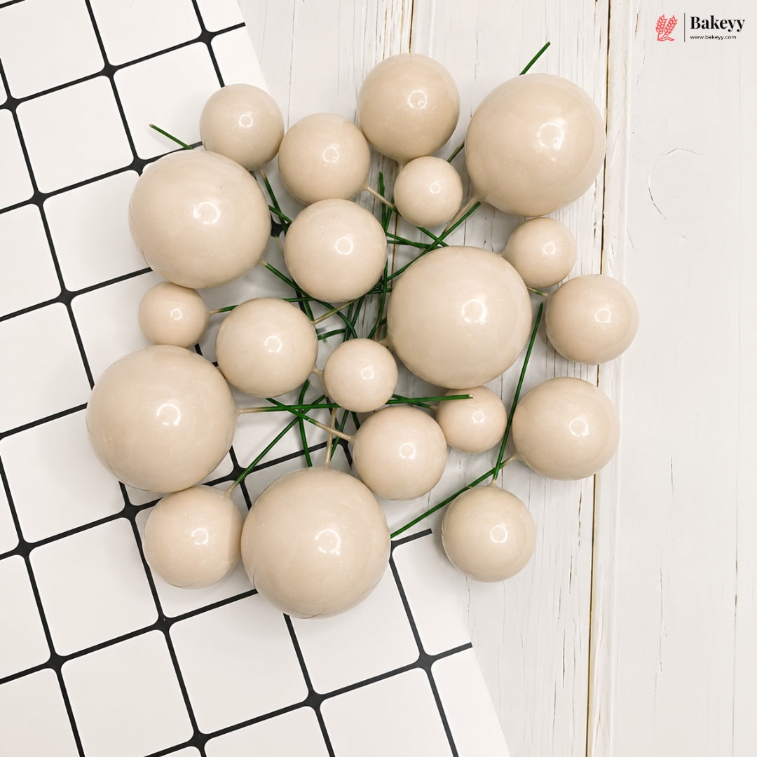 A cluster of glossy, beige faux pearlescent decorative beads with green stems, arranged on a split background of black-and-white checkered tiles and white wood planks. A 'flakeyy' brand logo is visible in the top right corner.