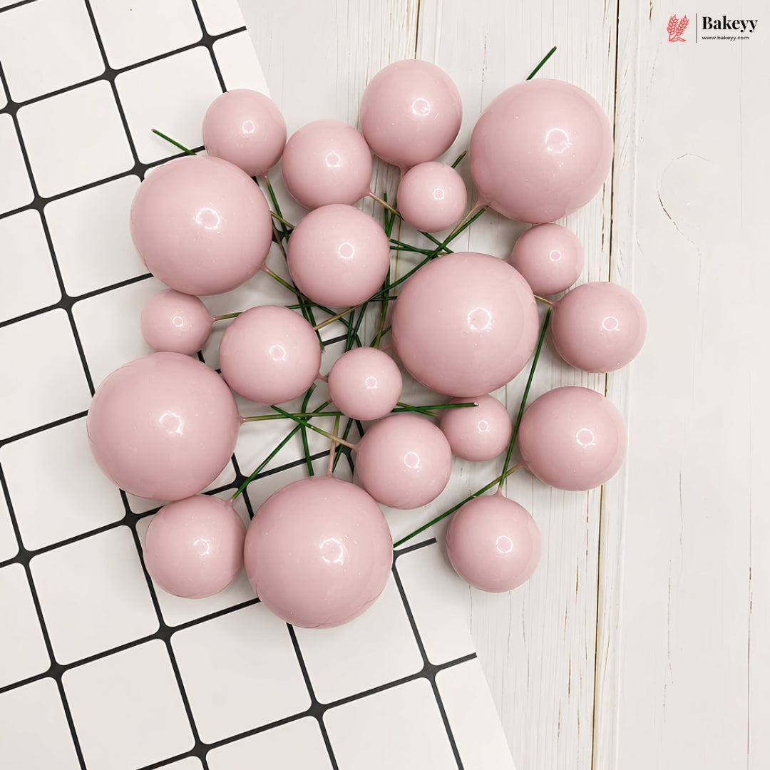 A cluster of glossy, pastel pink decorative pom-pom balls of various sizes, arranged on a white and black checkered tile surface with a white wood background. A 'flakeyeyy' brand logo is visible in the top right corner.