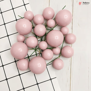 A cluster of glossy, pastel pink decorative pom-pom balls of various sizes, arranged on a white and black checkered tile surface with a white wood background. A 'flakeyeyy' brand logo is visible in the top right corner.