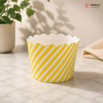 Yellow and white striped paper cupcake liner on a marble surface with a plant in the background.