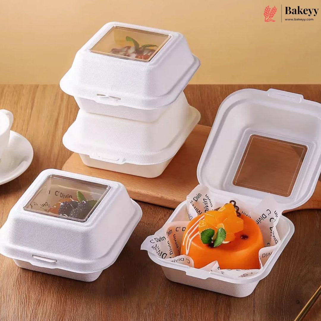 White biodegradable paper food containers with clear plastic lids, shown closed and open on a wooden table. One open container holds an orange dessert with mint garnish, and another shows a dark dessert inside.