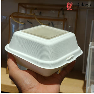 A hand holding a white biodegradable paper food container with a clear plastic lid, with a Bakeyy logo watermark in the top right corner.