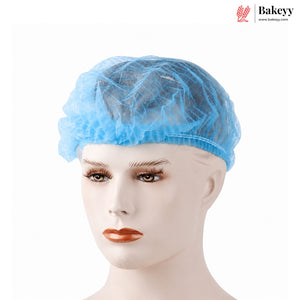 A light blue disposable non-woven bakery cap shown on a mannequin head against a plain white background, with the Bakeyy logo in the top right corner.