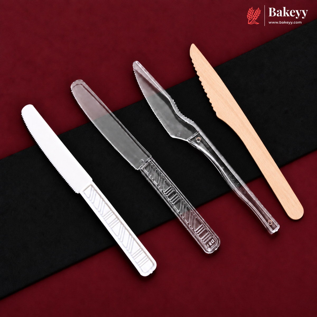 Four plastic cake and dessert knives in different colors (white, clear, silver, and light wood) arranged diagonally on a black and dark red background. The Bakeyy logo is visible in the top right corner.