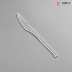 A single silver-colored plastic knife or spatula with a serrated blade and a long handle, shown diagonally on a solid gray background. The Bakeyy brand logo is visible in the top right corner.